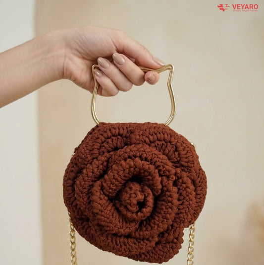 Brown rose-shaped handbag with gold chain handle held by a hand against a neutral background