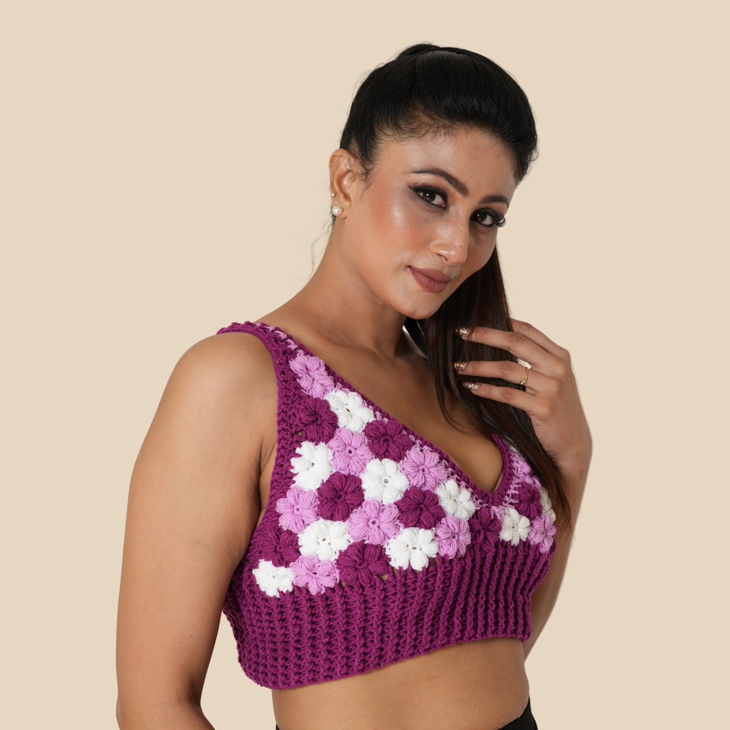 Woman wearing a purple crochet top with white floral patterns on a plain background