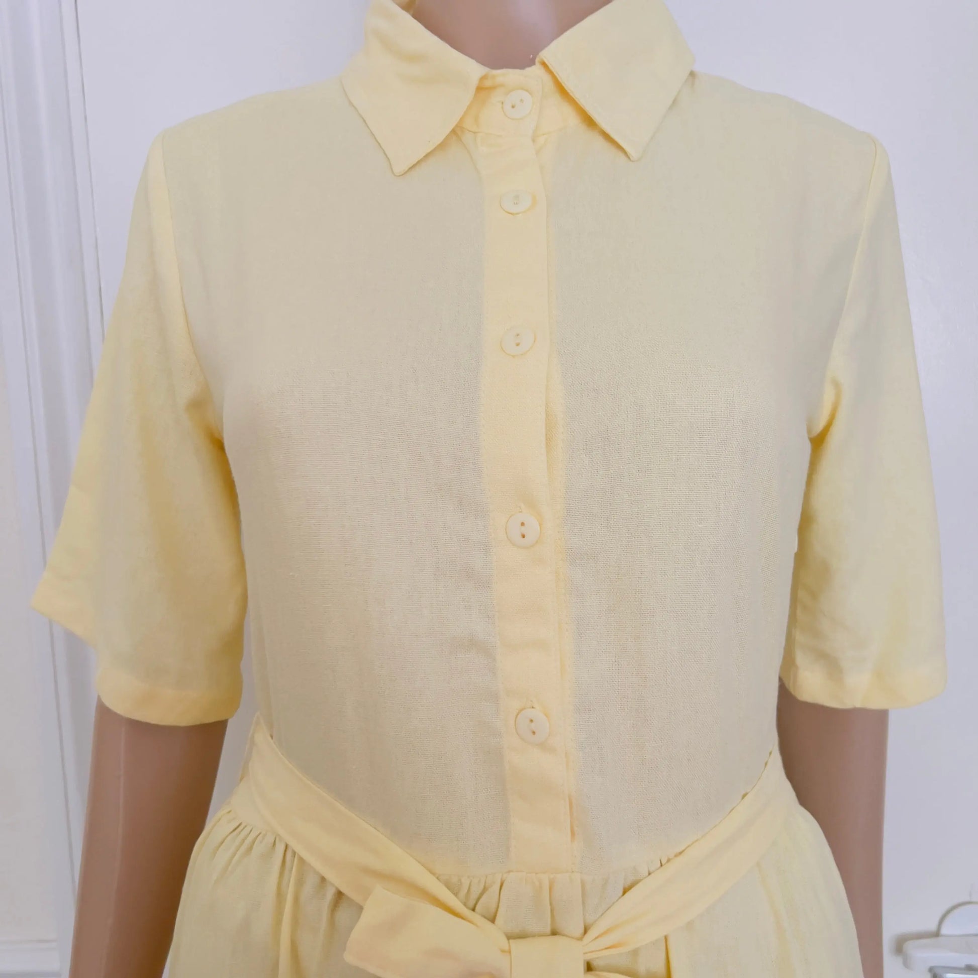 A pale yellow short-sleeve collared shirt dress displayed on a mannequin torso against a light indoor background.