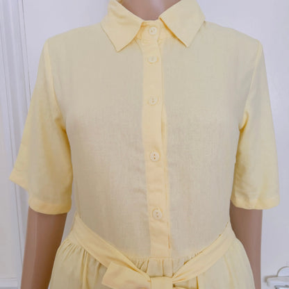 A pale yellow short-sleeve collared shirt dress displayed on a mannequin torso against a light indoor background.