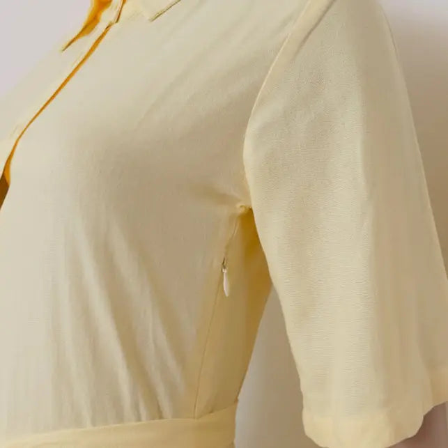 A close-up of a pale yellow short-sleeve collared top or dress, showing the fabric texture, collar, button placket, and a side zipper detail - Veyaro 