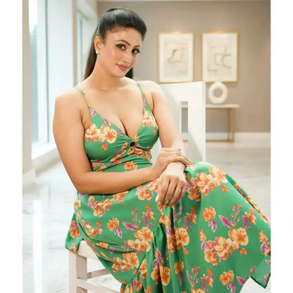 Woman in a green floral dress sitting on a white chair indoors.
