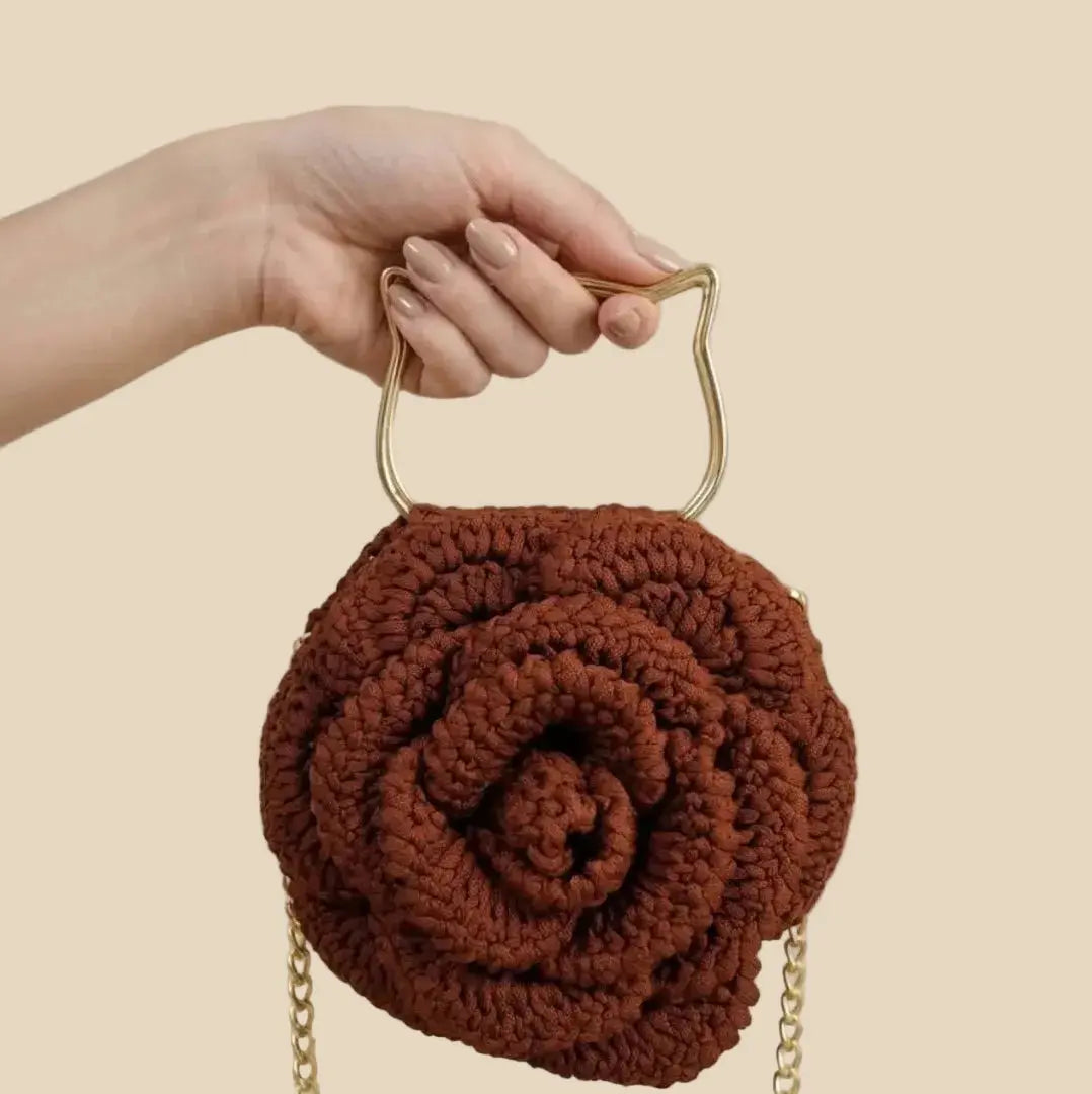 Brown rose-shaped handbag with gold chain handle held by a hand against a neutral background
