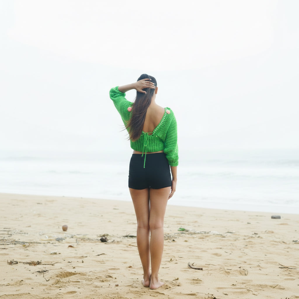 Person wearing a green crochet top with pink flowers on a beach-veyaro