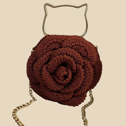 Brown handmade crochet bag with gold chain and handle on a textured surface.