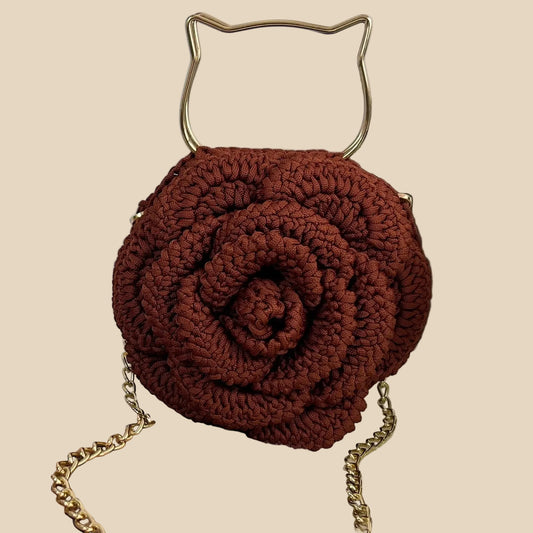 Brown handmade crochet bag with gold chain and handle on a textured surface.