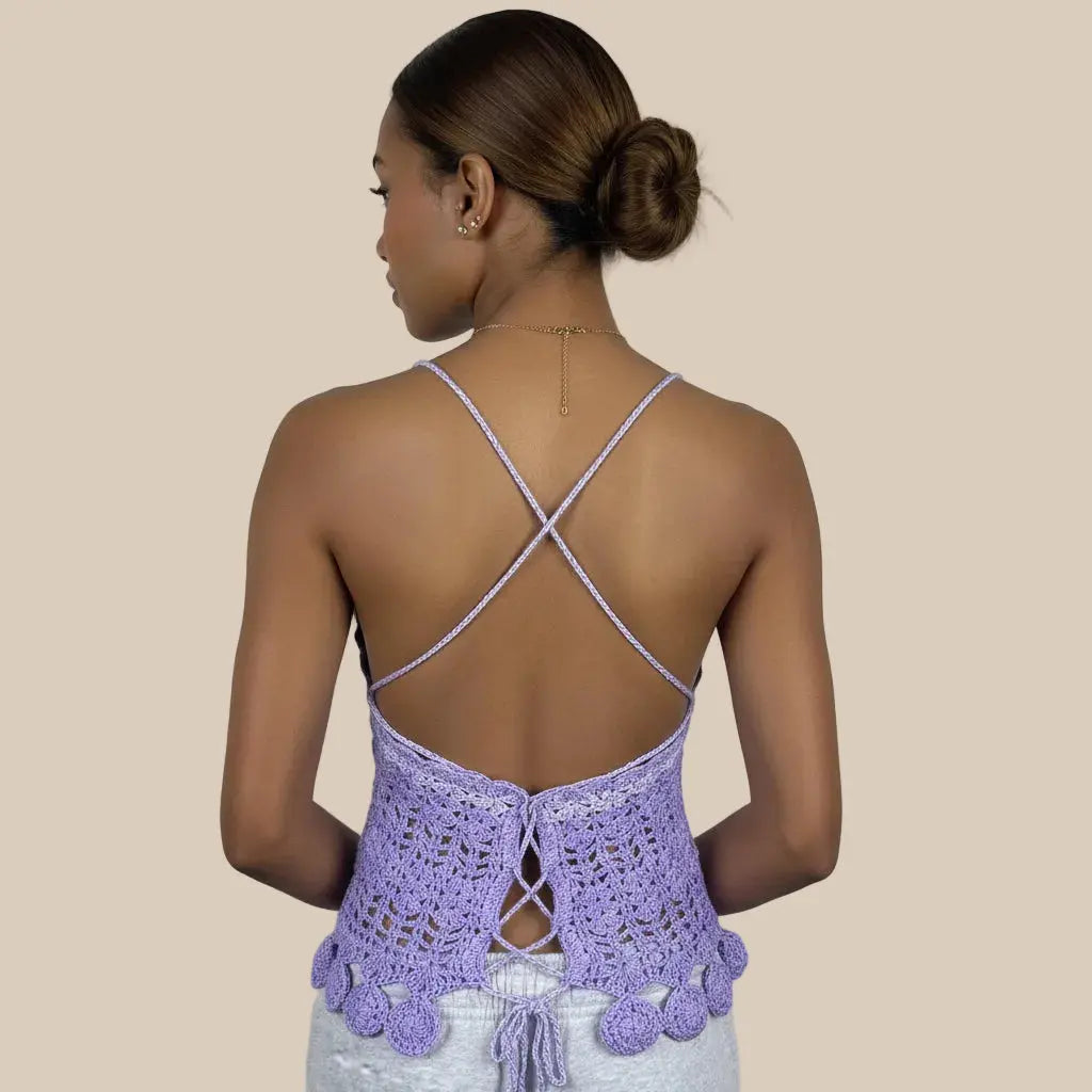 A woman shown from the back wearing a lavender crocheted open-back top with thin crisscross straps and scalloped trim, against a plain beige background - Veyaro
