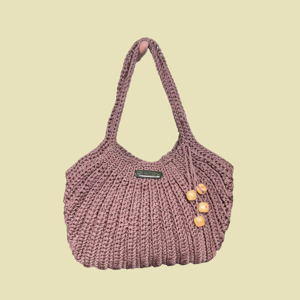 Knitted handbag with wooden buttons held by a person on a black leather couch.