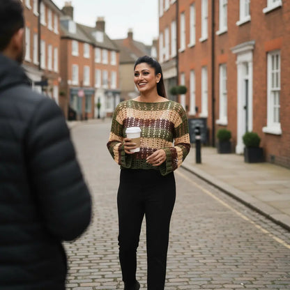 Woman in a patterned sweater holding a coffee cup on a street with brick buildings.