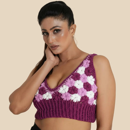 Woman wearing a purple crochet top with white floral patterns on a plain background