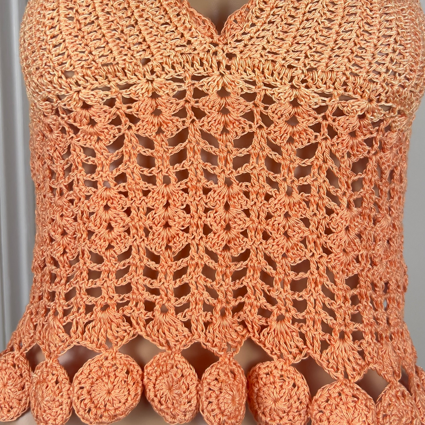 Close-up of a crocheted orange top with intricate patterns and pom-pom details.