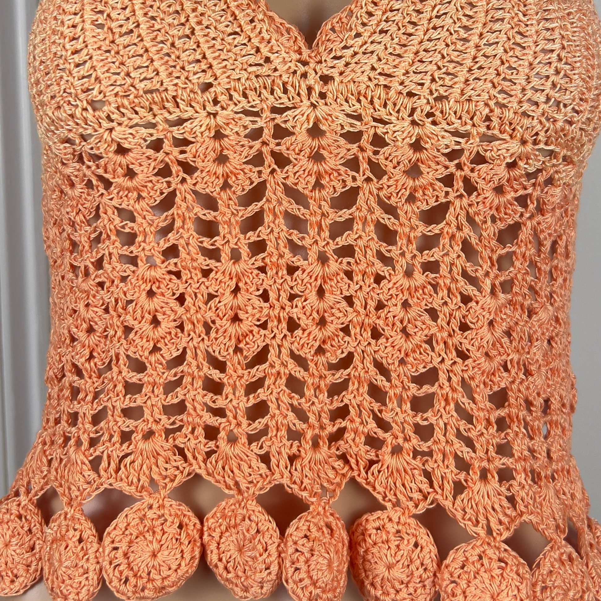 Close-up of a crocheted orange top with intricate patterns and pom-pom details.