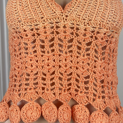 Close-up of a crocheted orange top with intricate patterns and pom-pom details.